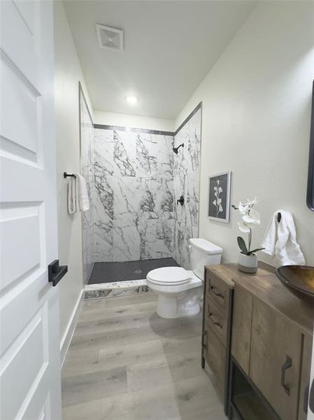 Bathroom featuring toilet, hardwood / wood-style floors, and a tile shower