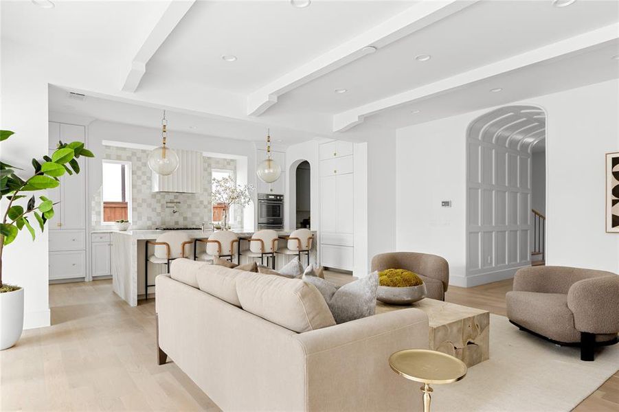 Living area with arched walkways, light wood-style floors, beam ceiling, and recessed lighting