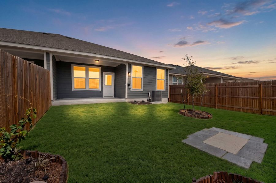 A fenced backyard features a covered concrete patio and lush green lawn at sunset. A fenced backyard features a covered concrete patio and lush green lawn at sunset.