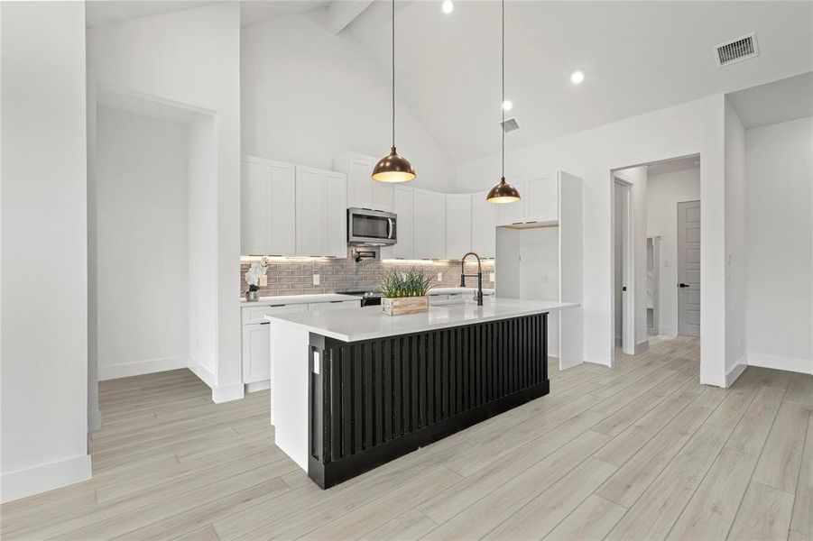Kitchen featuring stainless steel microwave, light countertops, backsplash, beamed ceiling, and light wood-type flooring