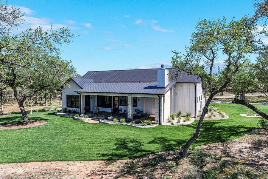 Rear view of house featuring a metal roof, a lawn, covered porch, stone siding, and a chimney