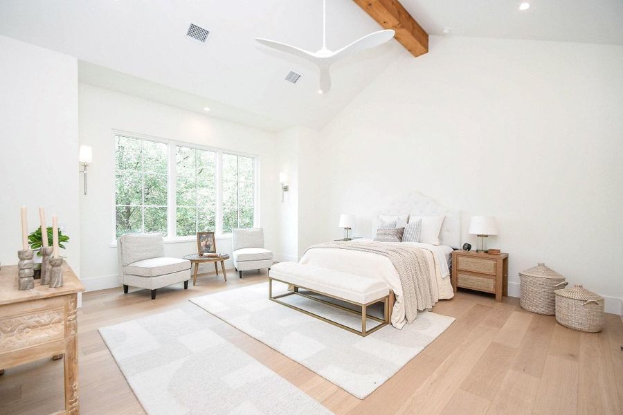 This bright and airy bedroom features a high ceiling with a wooden beam, large windows for natural light, and a minimalist design with neutral tones. It includes cozy seating, a stylish bed, and modern decor, creating a serene and inviting atmosphere.