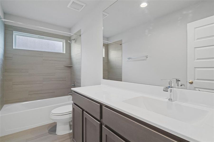 Secondary bath features tile flooring, bath/shower combo with tile surround, stained wood cabinets, beautiful light countertops, mirror, sleek fixtures and modern finishes.