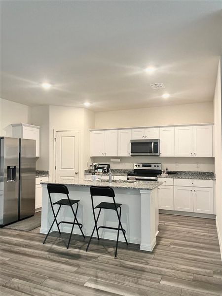 Kitchen featuring appliances with stainless steel finishes, white cabinets, light stone countertops, a breakfast bar, and light wood finished floors