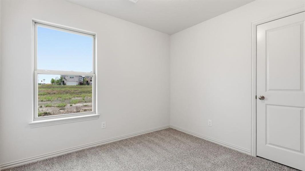 Bright interior room featuring a large single-hung window, light gray carpet flooring, white painted walls, white baseboards, and a white paneled door with a brushed nickel knob