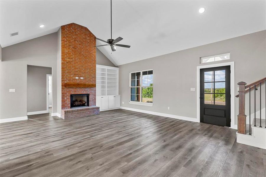 Unfurnished living room with built in shelves, high vaulted ceiling, a brick fireplace, and plenty of natural light