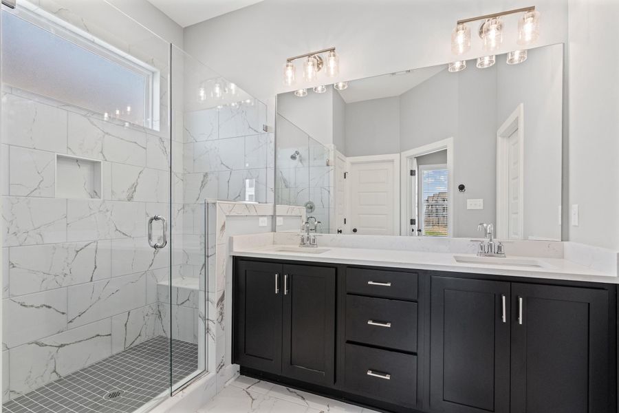 Bathroom featuring plenty of natural light, double vanity, a marble finish shower, and light marble finish floors