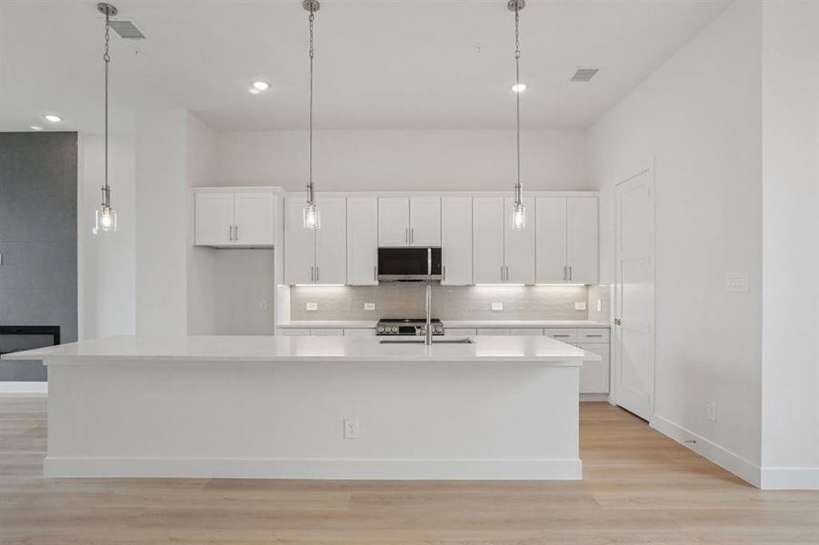 Kitchen featuring white cabinets, a spacious island, light wood finished floors, appliances with stainless steel finishes, and recessed lighting