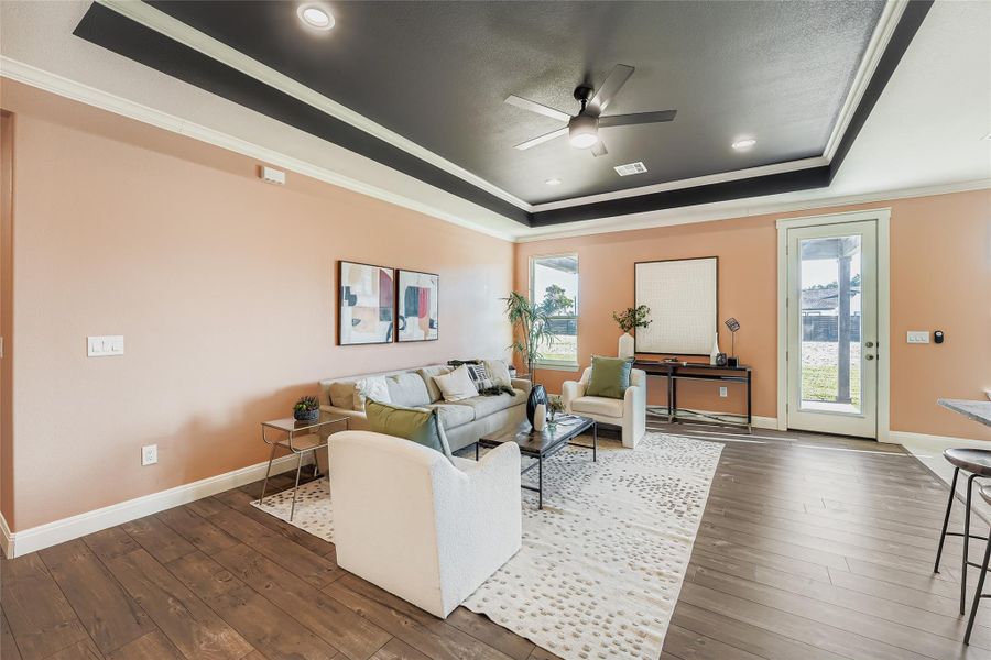 Living room with crown molding, a tray ceiling, dark wood finished floors, and a ceiling fan