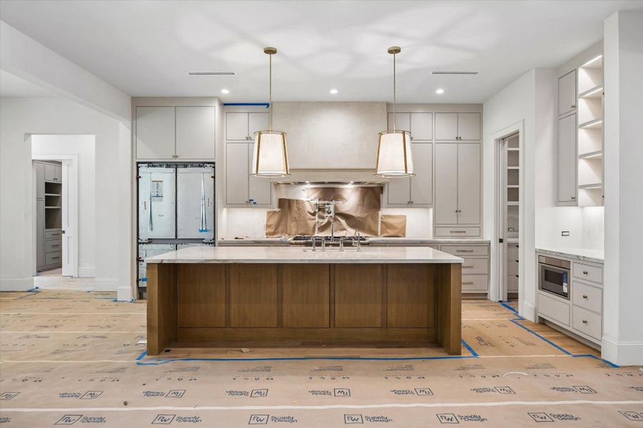 The kitchen boasts beautiful light fixtures, a white oak island, a plaster-finish vent hood, pot filler, and high-end appliances by Thermador. A built-in refrigerator is included, while the refrigerator, wine chiller, and dishwasher will be paneled to blend with the cabinetry. Site-built cabinets with soft-close mechanisms complete the space.