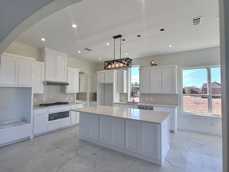 Kitchen with backsplash, decorative light fixtures, a kitchen island, white cabinets, and sink