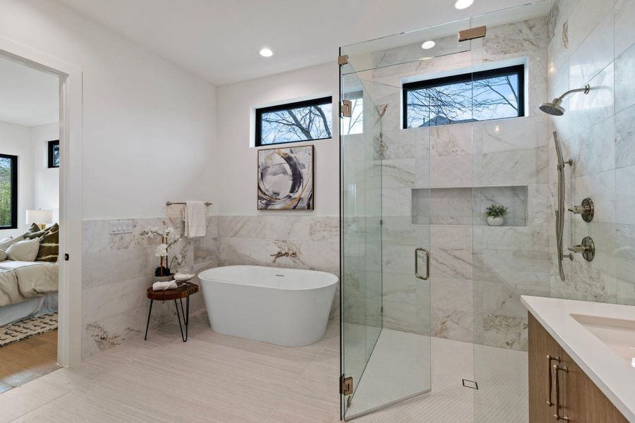 Ensuite bathroom featuring tile walls, a stall shower, a soaking tub, vanity, and a wainscoted wall