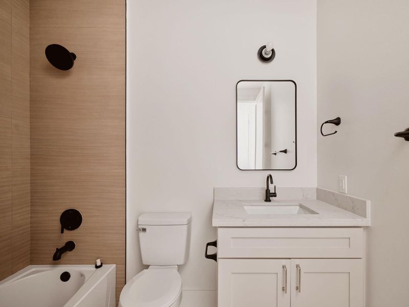 Bathroom featuring a light wood-finish tiled shower and tub surround, a white bathtub, a toilet, and a vanity with a light countertop