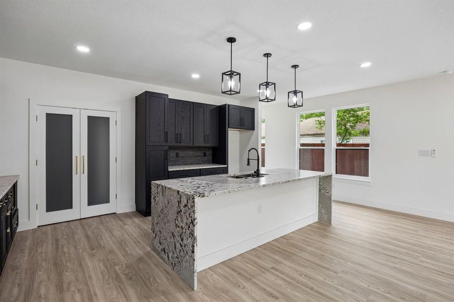 Modern kitchen featuring a waterfall island with a black sink and faucet Modern kitchen featuring a waterfall island with a black sink and faucet