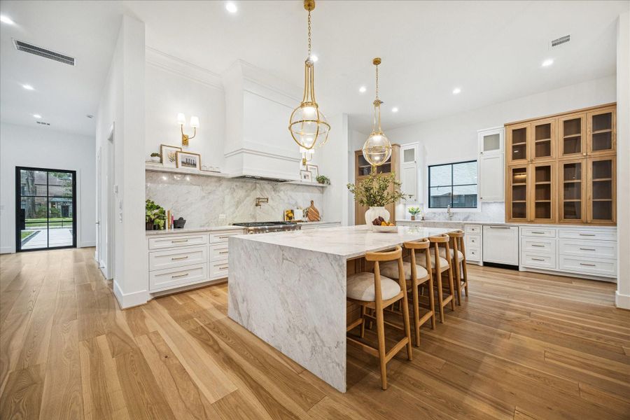 Full-height Montebello stone wraps the backsplash and hood with a sculptural presence. Custom cabinetry conceals storage and mechanicals, while a brass pot filler adds function and refinement. Tankless water heater and pre-plumbing for a future water softener support long-term performance.