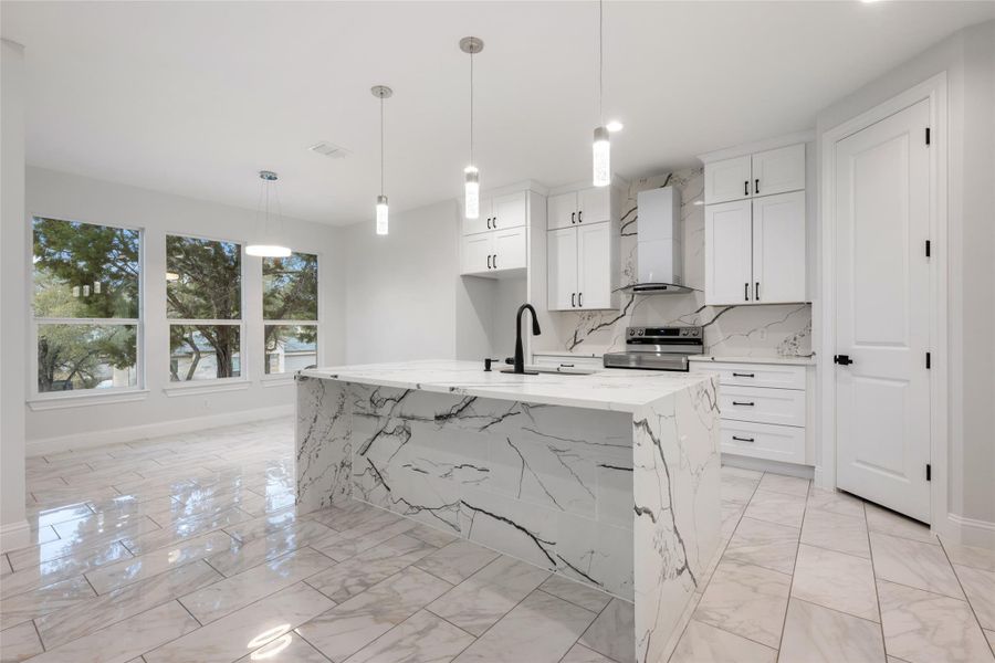 Kitchen with light stone counters, stainless steel range with electric cooktop, decorative light fixtures, and white cabinetry