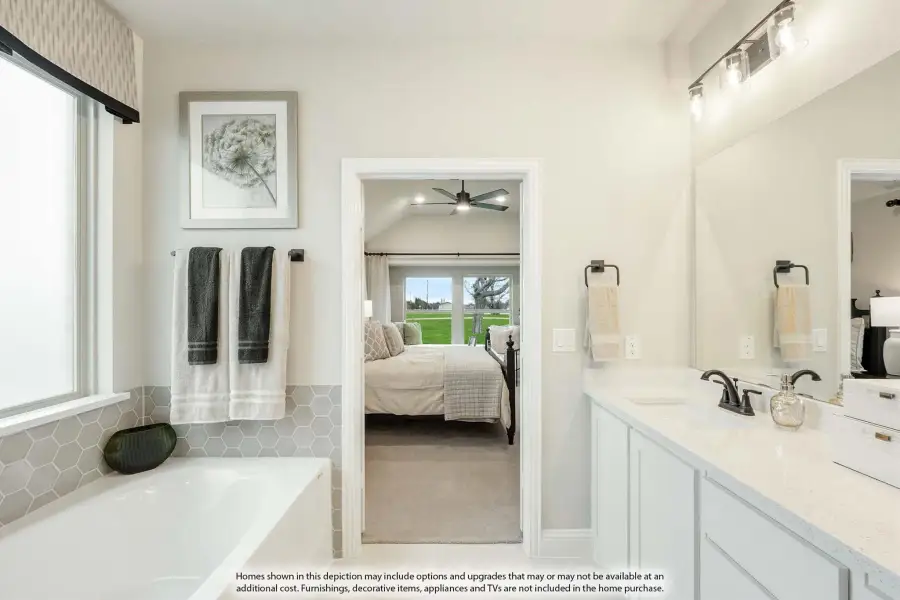 Ensuite bathroom with soaking tub, white vanity, and open doorway to master bedroom with vaulted ceiling