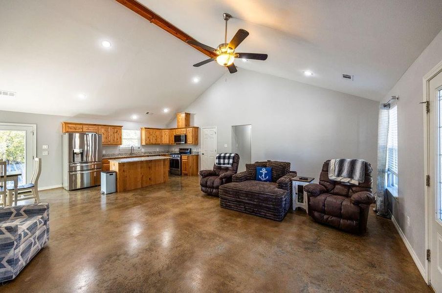 Living room with healthy amount of natural light, high vaulted ceiling, a ceiling fan, and finished concrete flooring
