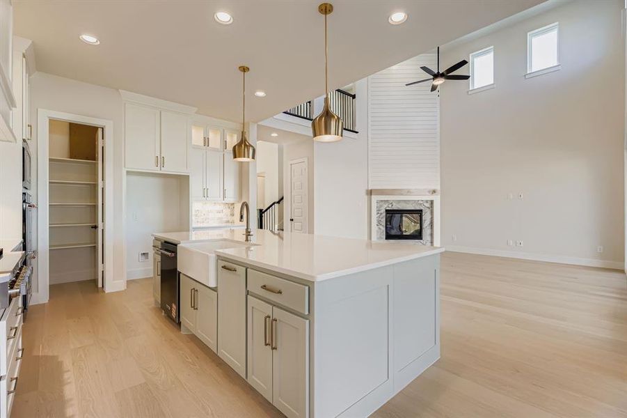 Kitchen featuring a kitchen island with sink, light wood-style floors, a multi sided fireplace, white cabinets, and pendant lighting