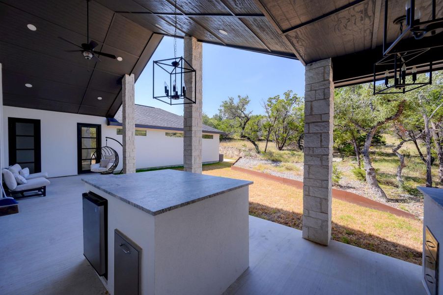 Stone pillars support a covered patio complete with an outdoor kitchen overlooking natural wooded terrain.