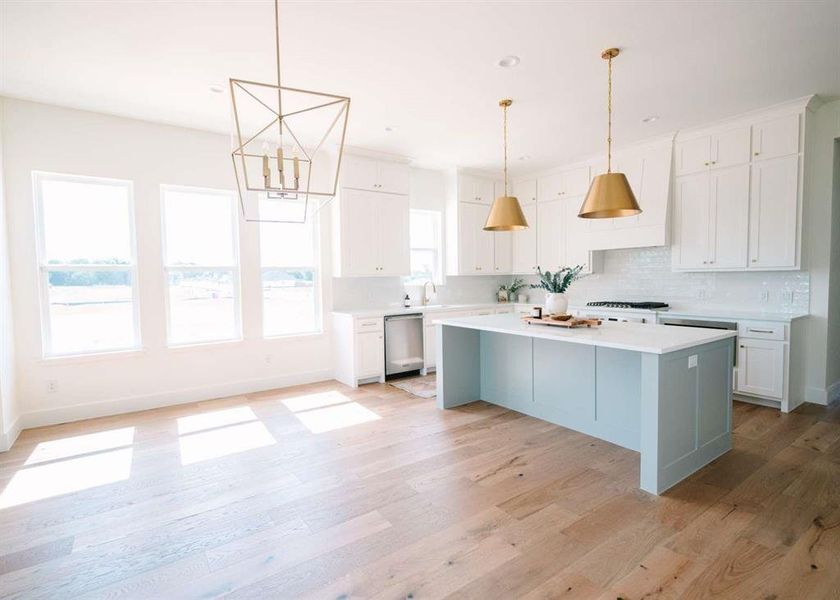Kitchen featuring decorative light fixtures, light hardwood / wood-style floors, a kitchen island, white cabinetry, and stainless steel dishwasher