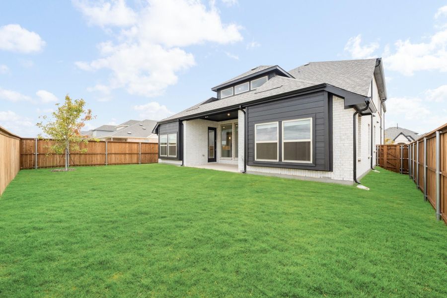 Rear exterior of two-story home with white brick, dark siding, covered patio, and fenced backyard with green lawn.