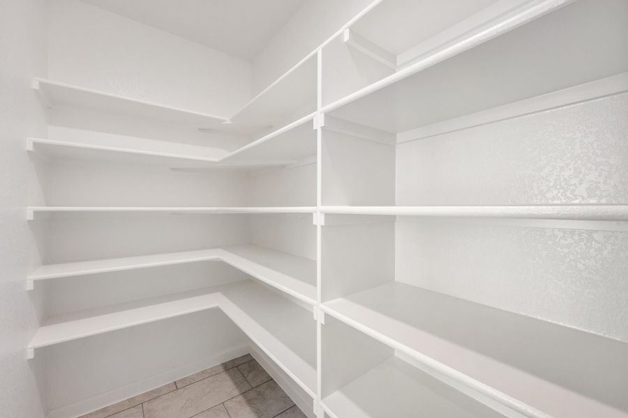 Walk-in pantry with white wrap-around shelving and tile floor