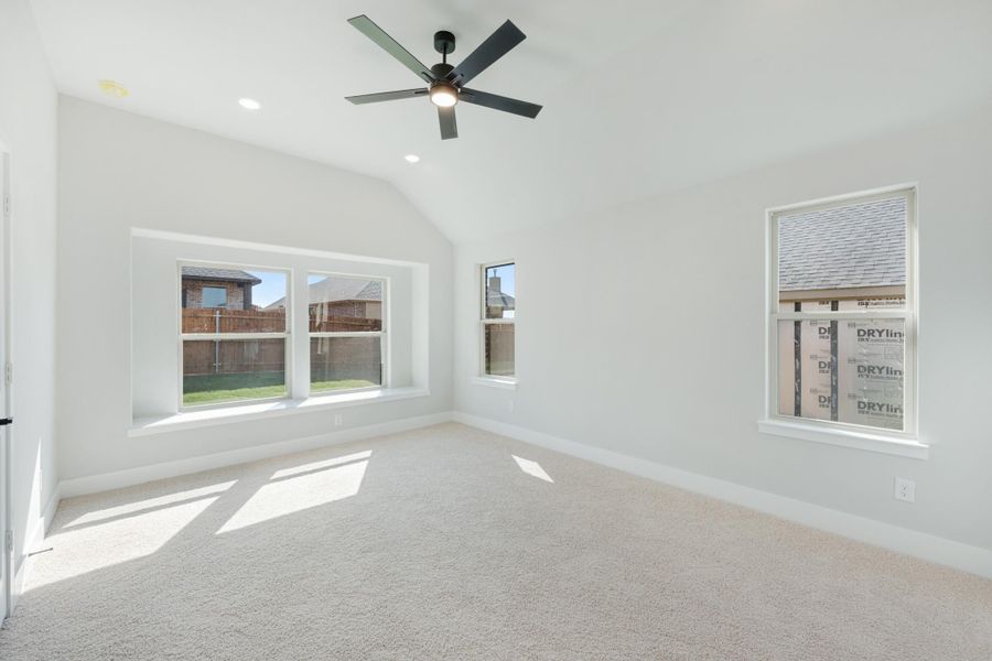 Empty bedroom with vaulted ceiling, ceiling fan, carpet flooring, and multiple windows