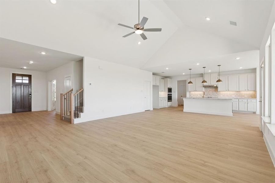 Unfurnished living room featuring recessed lighting, light wood-style flooring, high vaulted ceiling, a ceiling fan, and stairs