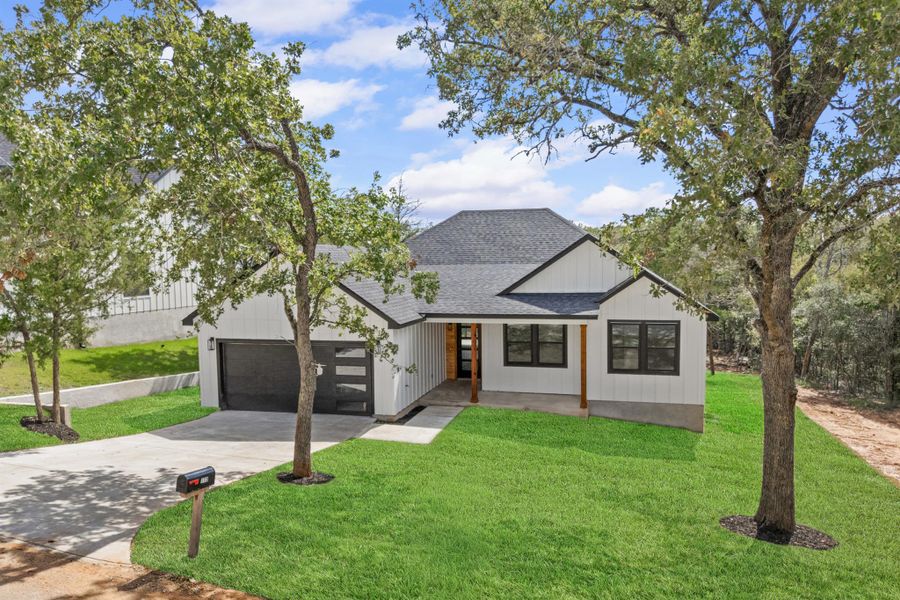 Modern inspired farmhouse featuring a shingled roof, driveway, a front lawn, a garage, and covered porch