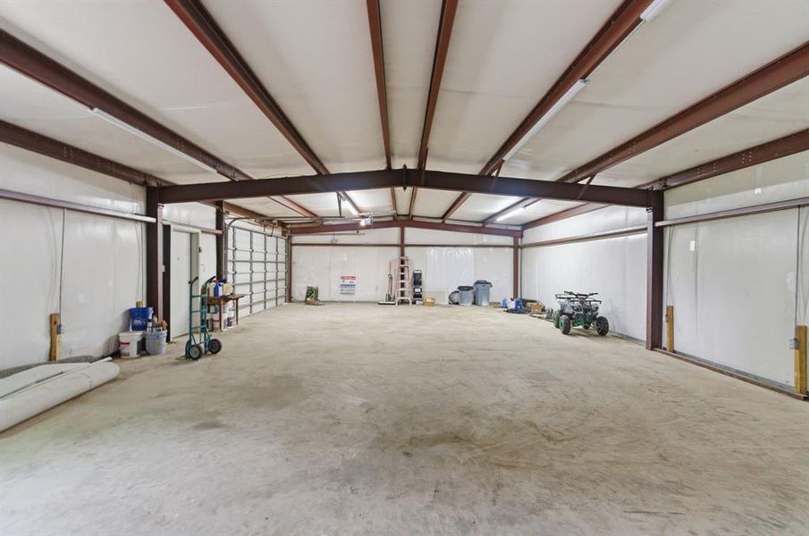 Expansive interior space featuring a concrete floor, exposed structural beams, and overhead lighting Expansive interior space featuring a concrete floor, exposed structural beams, and overhead lighting