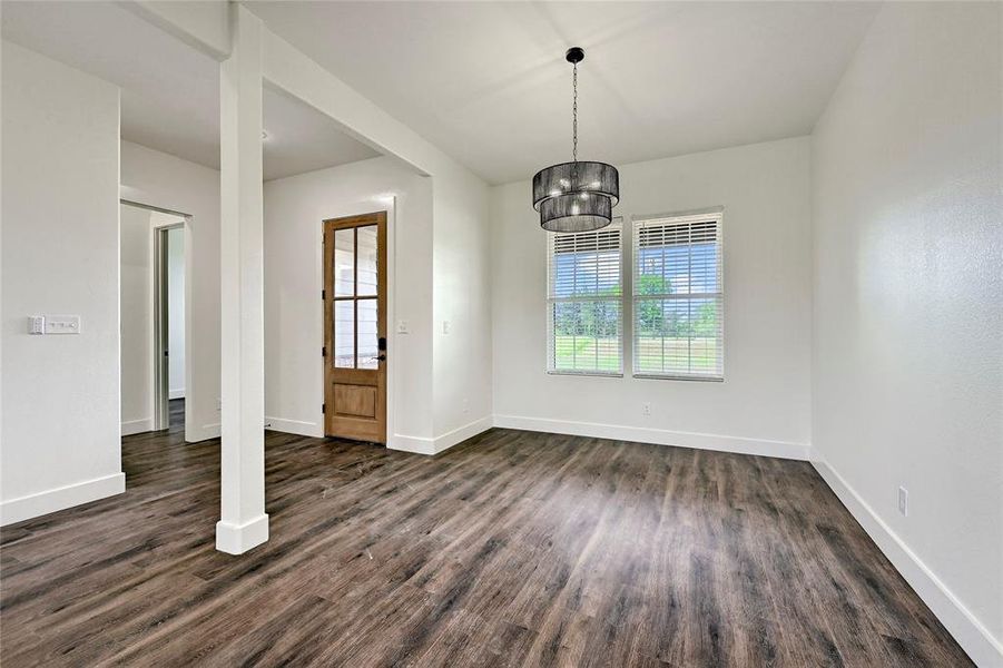 Unfurnished dining area featuring a chandelier, baseboards, and dark wood finished floors