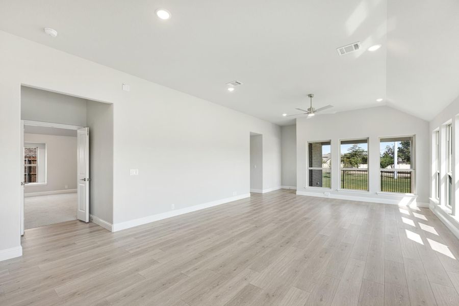 Open living room with vaulted ceiling, ceiling fan, light wood floors, and large windows overlooking a patio