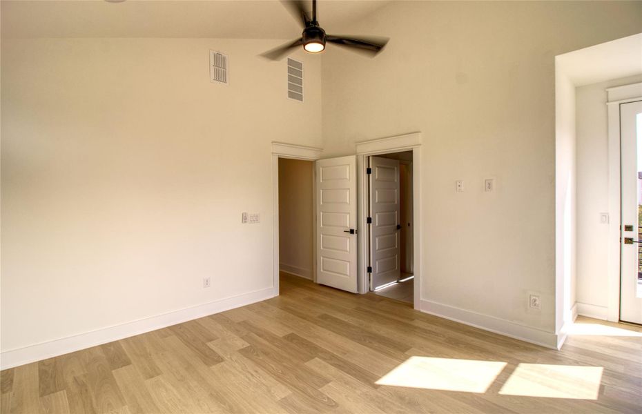 Primary bedroom featuring light wood-style floors, a ceiling fan, and a towering ceiling
