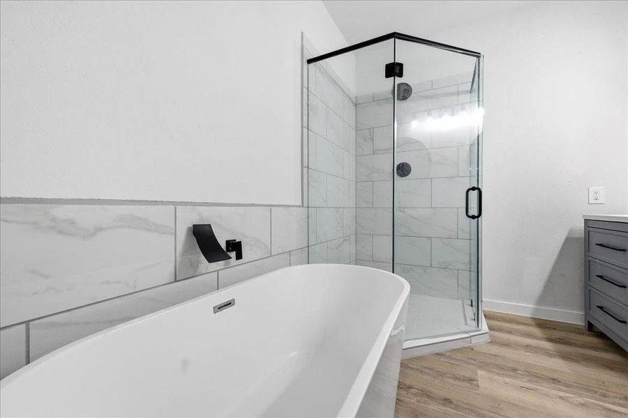 Modern tile details surround the luxury primary bathroom tub and frameless shower setup. Modern tile details surround the luxury primary bathroom tub and frameless shower setup.