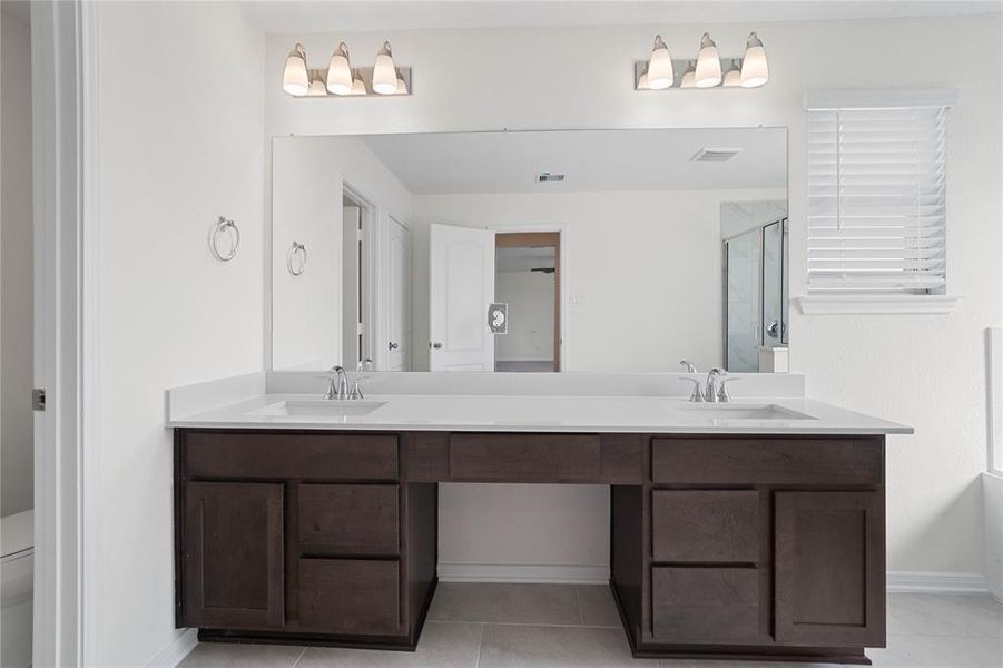 This primary bathroom is definitely move-in ready! Featuring a framed walk-in shower with tile surround, separate garden tub for soaking after a long day with custom tile detailing, dark stained cabinets with light countertops and dual vanities, high ceilings, custom paint, sleek and modern finishes.