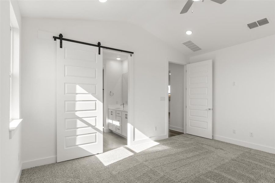 Unfurnished bedroom featuring visible vents, a barn door, light carpet, and vaulted ceiling