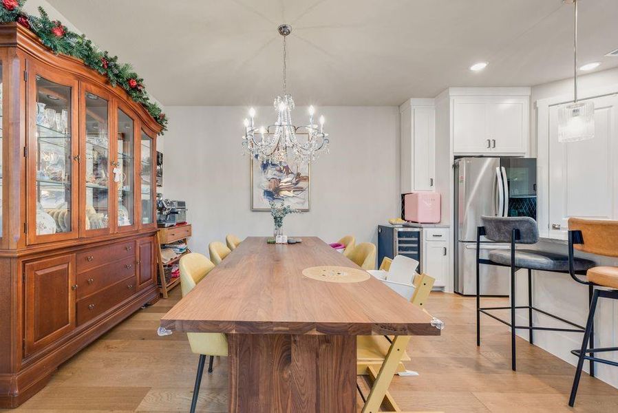 Dining area with light wood-style flooring, suspended lighting, and wine cooler