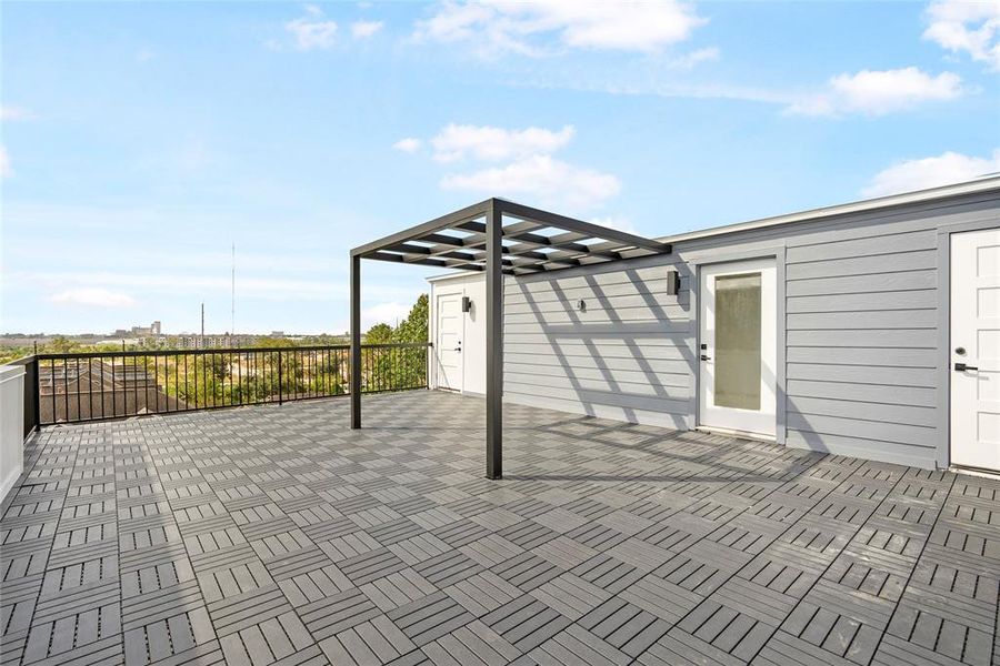 This is a spacious rooftop terrace with modern grey decking, a pergola, and scenic views, perfect for outdoor relaxation and entertaining.