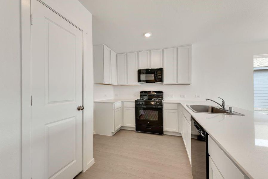 Kitchen with black appliances, light wood finished floors, a sink, and light countertops