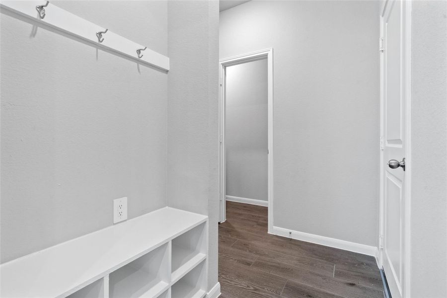 Across from the kitchen is this dedicated area features a custom built-in bench with hooks, perfect for organizing coats, bags, and shoes right off the main hallway, keeping the rest of the home tidy.