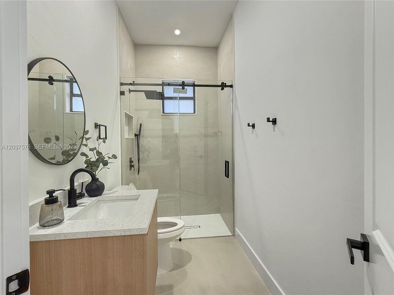Bathroom featuring a wood-finish vanity with an integrated white sink and speckled countertop, a matte black faucet, and a large circular mirror