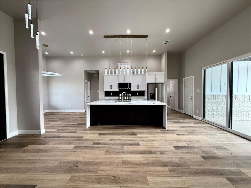 Kitchen featuring a large island with sink, pendant lighting, open floor plan, white cabinets, and recessed lighting