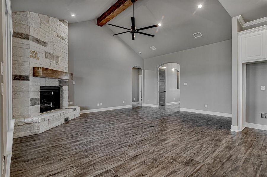 Unfurnished living room with ceiling fan, beamed ceiling, a stone fireplace, and high vaulted ceiling