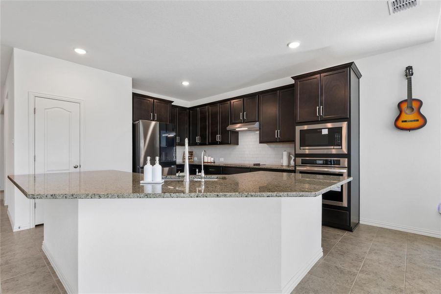 A well-appointed culinary space featuring dark cabinetry and a spacious granite-topped island with a sink. A well-appointed culinary space featuring dark cabinetry and a spacious granite-topped island with a sink.