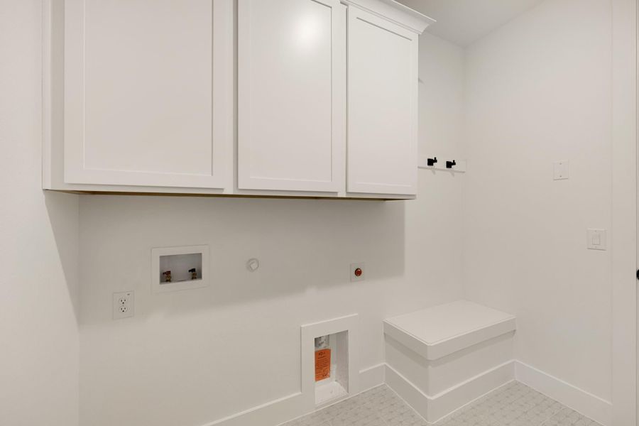 Laundry room with white upper cabinets, washer hookups, wall hooks, and a small built-in bench on tile floor