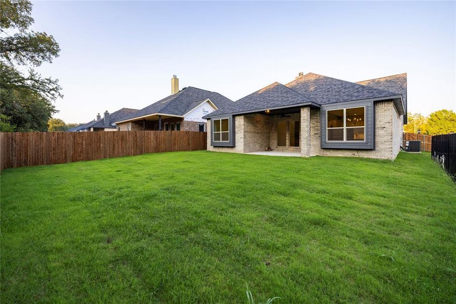 Rear view of property featuring brick siding, a fenced backyard, a patio area, and a shingled roof