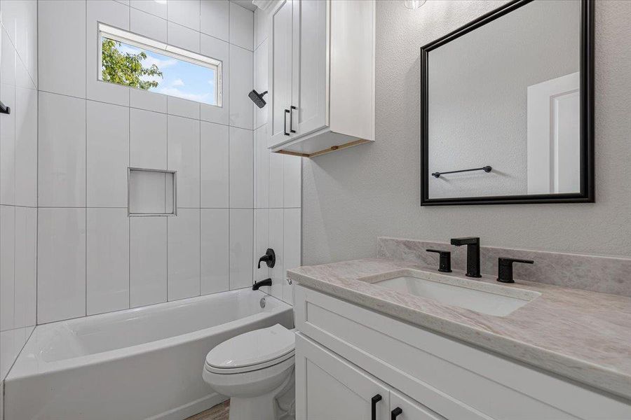 Guest bathroom with stone countertop, tiled shower, and modern fixtures!