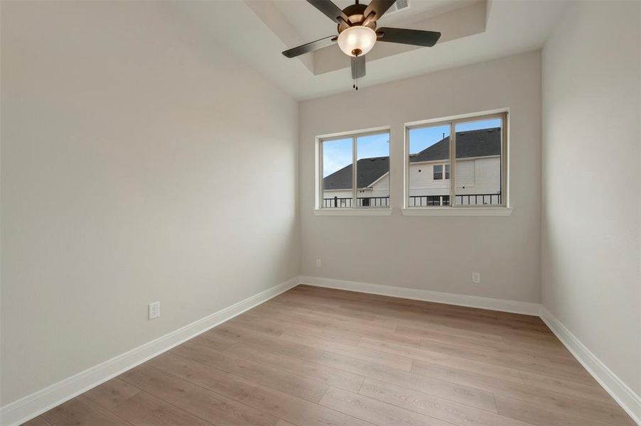 Empty room featuring light wood-style flooring, a tray ceiling, and ceiling fan