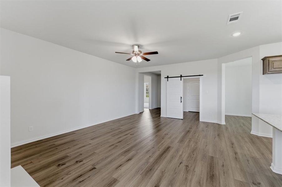 Spacious room featuring wood-finish flooring, a ceiling fan with integrated lighting, and a modern white barn door